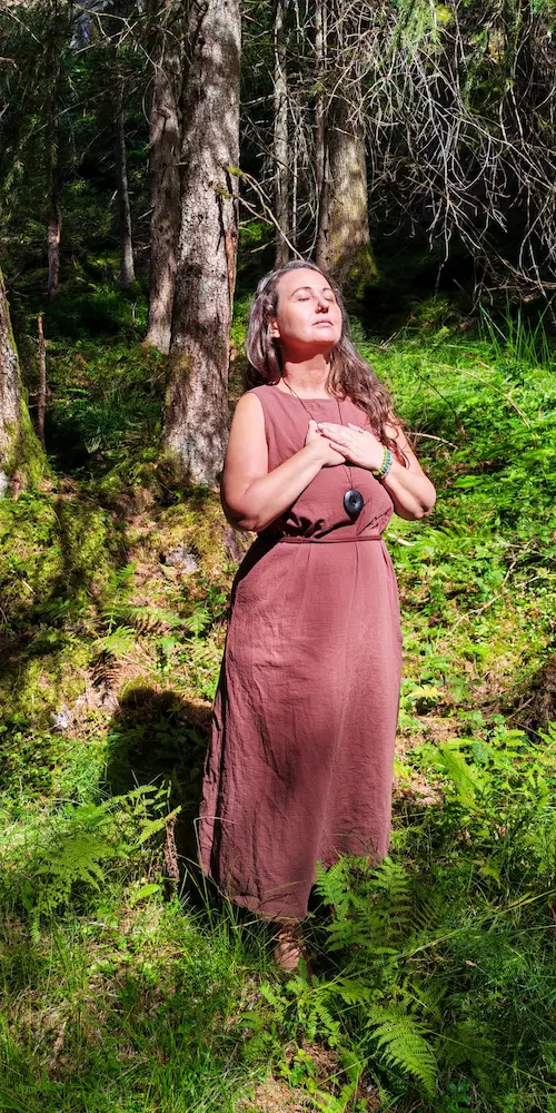 Übermich Über mich - stehend im Wald, Hände auf dem Herz und das Gesicht der Sonne zugewandt